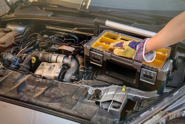 Caja de herramientas con la mano en el motor del coche de cerca