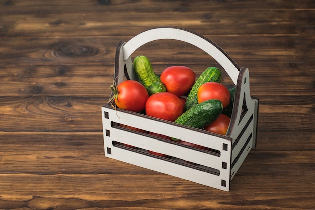 Una caja llena de pepinos y tomates sobre una mesa de madera.