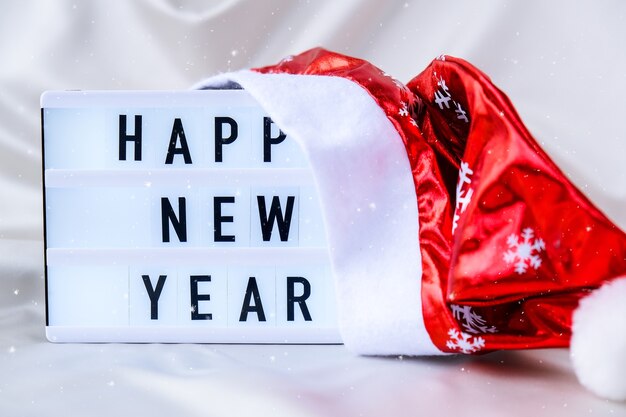 Caja de luz con texto feliz año nuevo con sombrero de santa sobre fondo de tela de seda concepto de vacaciones de invierno