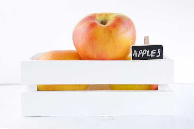 Caja de madera blanca llena de manzanas frescas y una pequeña pizarra aislada en un fondo blanco