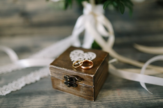 Caja de madera cerrada con corazón y anillos de oro para los novios