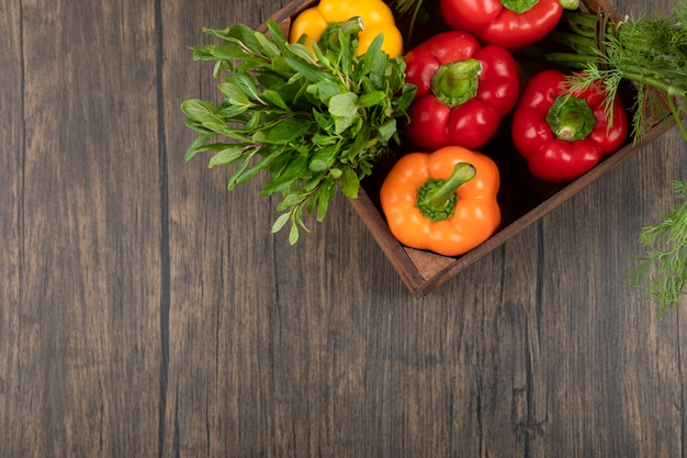 Caja de madera de coloridos pimientos y verduras sobre superficie de madera