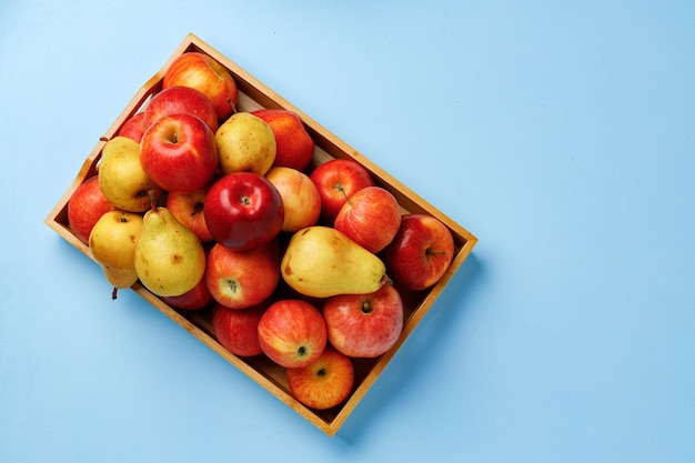 Caja de madera con manzanas y peras sobre fondo azul.