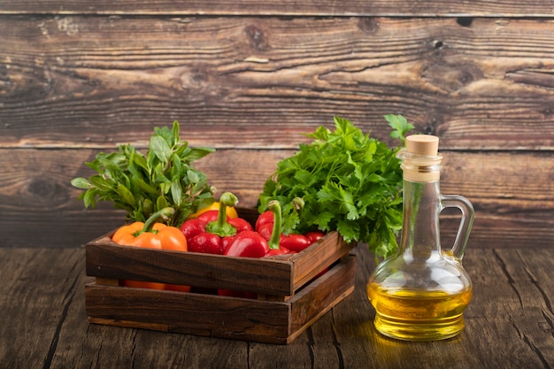 Caja de madera de pimientos frescos y aceite de oliva sobre superficie de madera