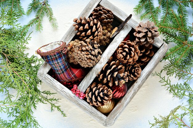 Caja de madera con piñas y juguetes navideños con ramas de abeto sobre un fondo azul claro