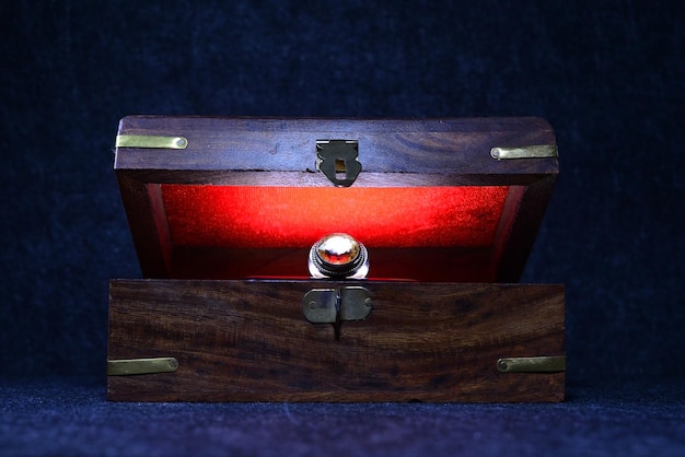 Caja de madera retro antigua entreabierta con un anillo de joyería y una luz roja en su interior sobre un fondo oscuro