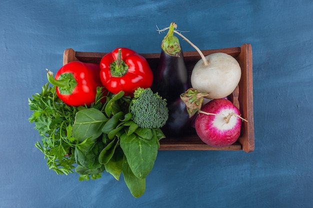 Caja de madera de verduras y verduras frescas y saludables en la superficie azul.