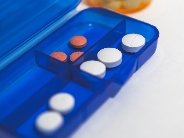 Foto caja de medicación azul con pastillas en el interior sobre fondo blanco.