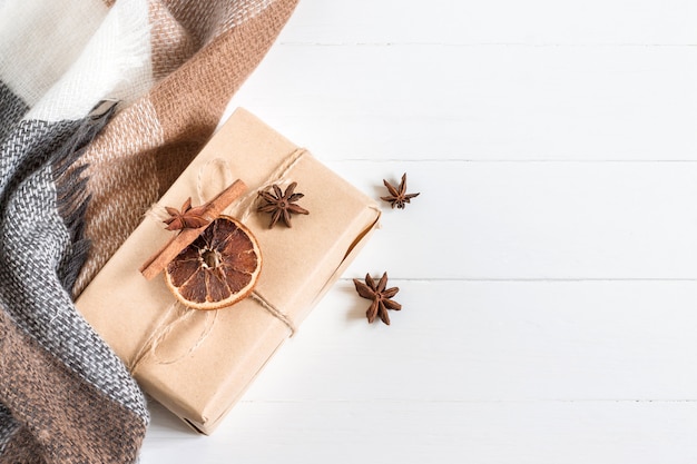 Caja de Navidad con un regalo en papel artesanal, una bufanda, una tela escocesa, conos, anís en una madera blanca en una vista superior de estilo rústico, copyspace. Año nuevo y navidad