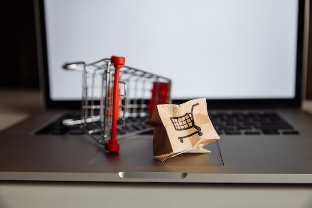 Caja de papel dañada y carrito de compras en un teclado de computadora portátil. Concepto de entrega. Accidente de envío.