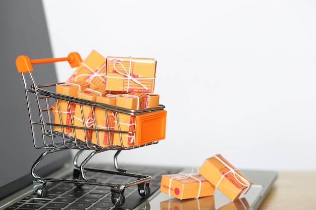 Caja de paquete marrón y modelo de carro de compras en miniatura en el teclado de la computadora