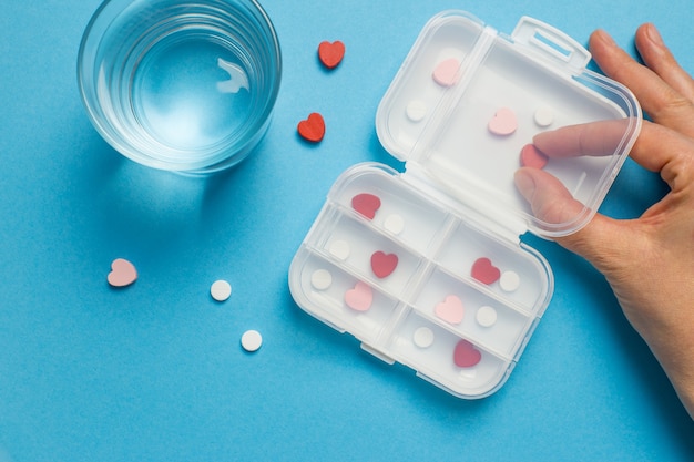 Una caja de pastillas y un vaso de agua sobre un fondo azul.