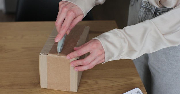 Caja de pedido de corte de consumidor de mujer en la mesa en la habitación de la casa Vista de cerca de la mujer corta cartón y usa un cuchillo en la mano Cliente feliz del concepto de minorista en línea