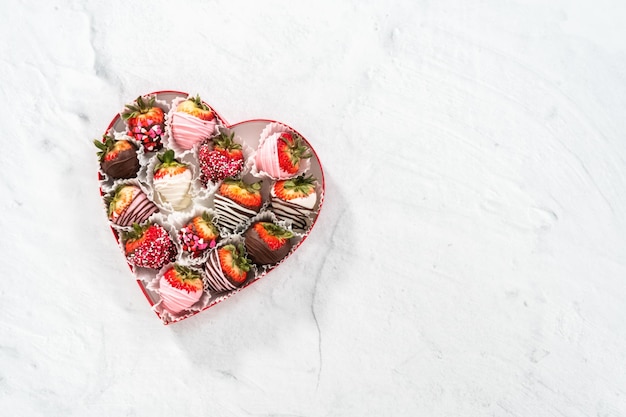 Caja plana en forma de corazón con una variedad de fresas cubiertas de chocolate sobre un fondo blanco