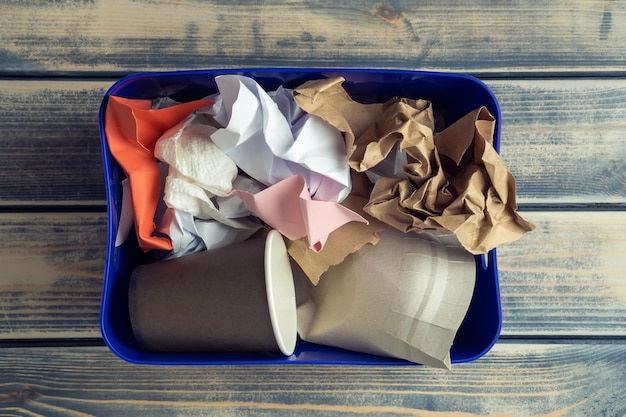 Caja de plástico azul llena de basura de papel arrugado sobre fondo de madera Crisis de prevención del calentamiento global