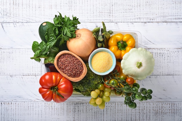 Caja de plástico con surtido de verduras frescas, frutas, cereales y semillas sobre fondo de madera vieja. Entrega a domicilio segura, cocción de alimentos y fondo de alimentos saludables y limpios y maquetas.