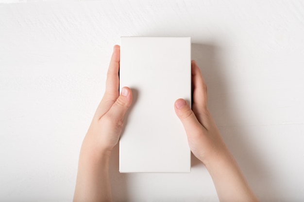 Caja rectangular de cartón blanca en manos de niños.