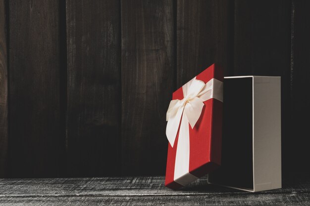 Caja de regalo abierta sobre una mesa de madera oscura. caja roja con cinta blanca