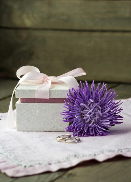 Caja de regalo con anillos de boda y una flor sobre la mesa.