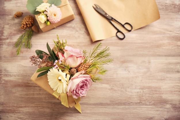 Caja de regalo artesanal con flores y tijeras sobre mesa de madera