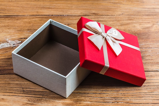 La caja de regalo ató la cinta roja con los pequeños corazones rojos impresos en él. Sobre fondo de madera vieja.