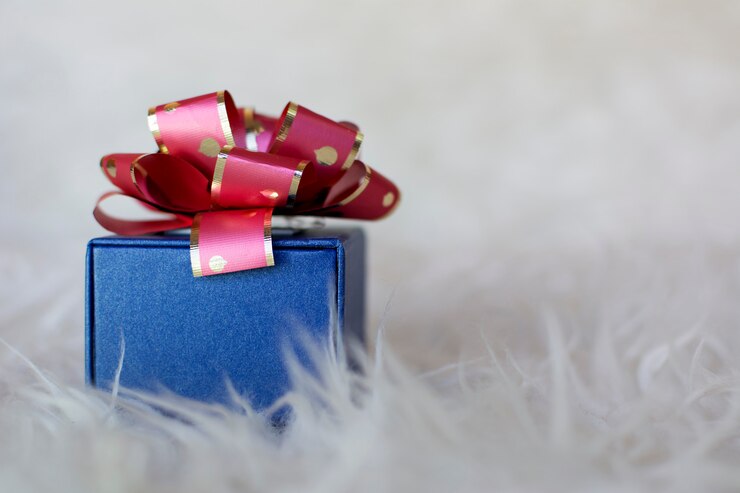 Caja de regalo azul con lazo rojo, aislado sobre fondo blanco peludo. Copyspace a la derecha.
