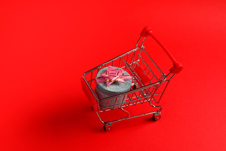 Foto caja de regalo azul con lazo rosa en un carrito de compras sobre un fondo rojo.