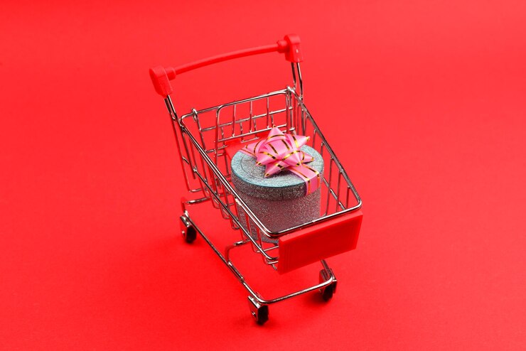 Foto caja de regalo azul con lazo rosa en un carrito de compras sobre un fondo rojo.