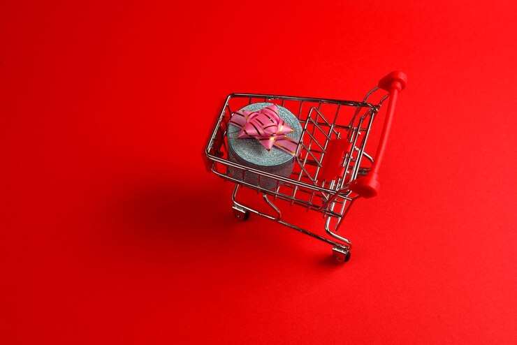 Foto caja de regalo azul con lazo rosa en un carrito de compras sobre un fondo rojo.