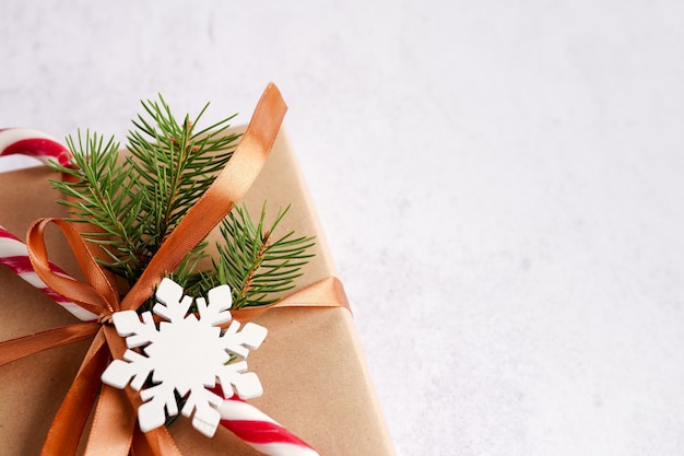 Caja de regalo con bastón de caramelo, lazo dorado y copo de nieve de madera sobre fondo blanco, espacio de copia