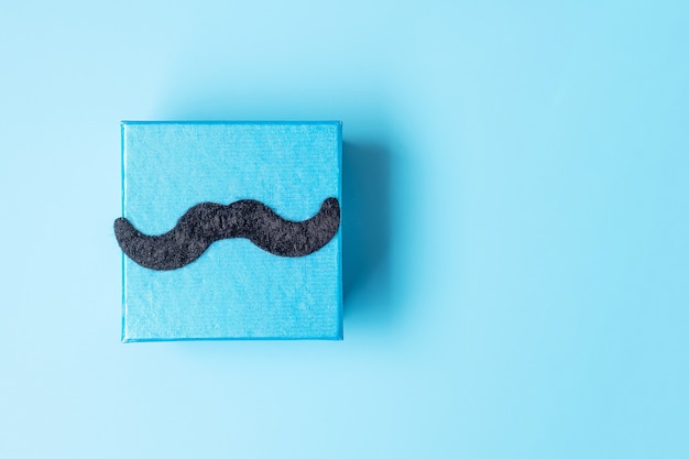 Caja de regalo con bigote sobre fondo azul, preparación para padres. concepto del día mundial del hombre y del día del padre