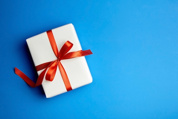 Caja de regalo blanca atada con cinta roja sobre azul