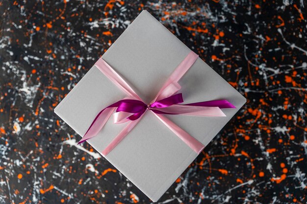 Caja de regalo blanca atada con una cinta roja sobre un fondo de color manchado