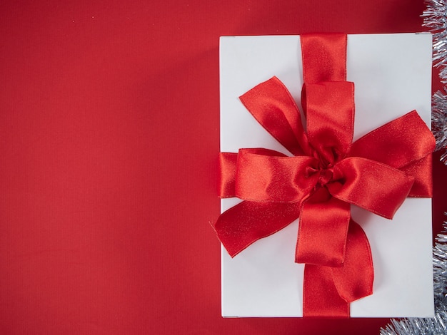 Caja de regalo blanca con cinta roja sobre fondo rojo.