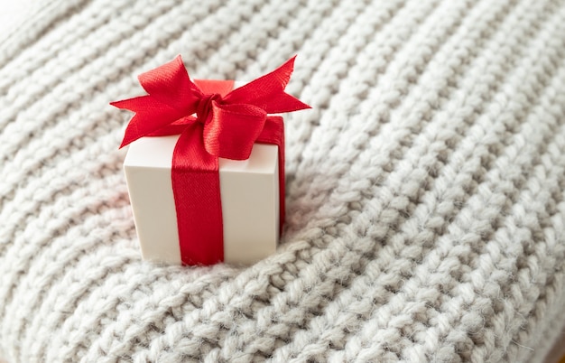 Caja de regalo blanca con cinta roja en suéter de punto beige