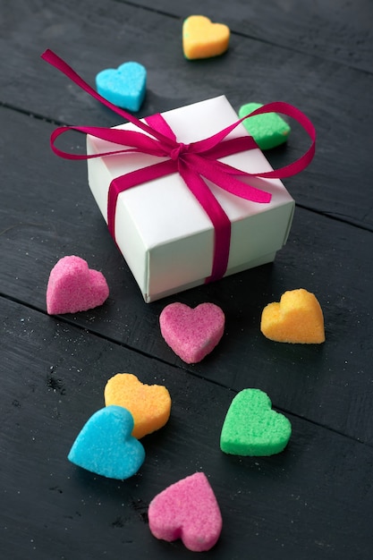 Caja de regalo blanca con una cinta rosa junto a corazones de azúcar de colores. Concepto del día de San Valentín