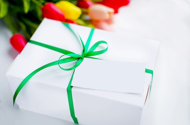 Caja de regalo blanca con cinta verde y ramo de tulipanes amarillos