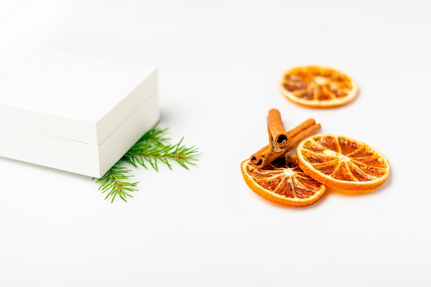 Caja de regalo blanca con frutos secos de naranja y canela sobre fondo blanco.