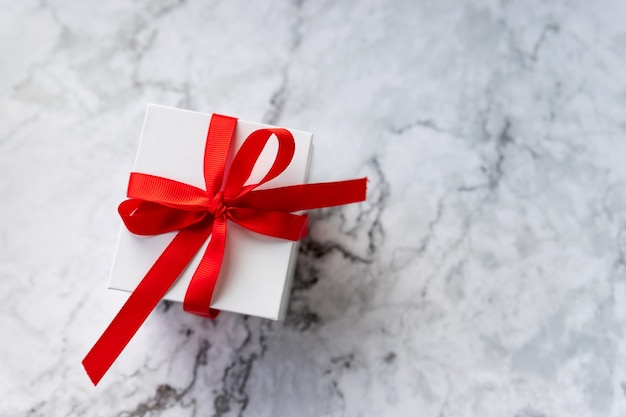 Caja de regalo blanca con lazo de cinta roja sobre fondo de mármol vacaciones y concepto de celebración espacio de copia presente para celebrar la Navidad de San Valentín o un aniversario