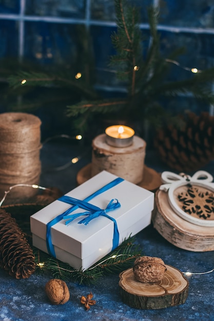 Caja de regalo blanca de navidad con lazo azul, cinta, adornos de madera, velas, nueces