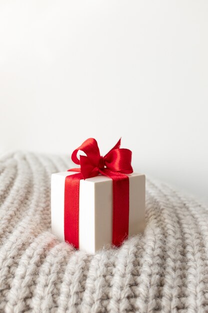 Caja de regalo blanca de primer plano con lazo de cinta roja en suéter de punto cálido beige