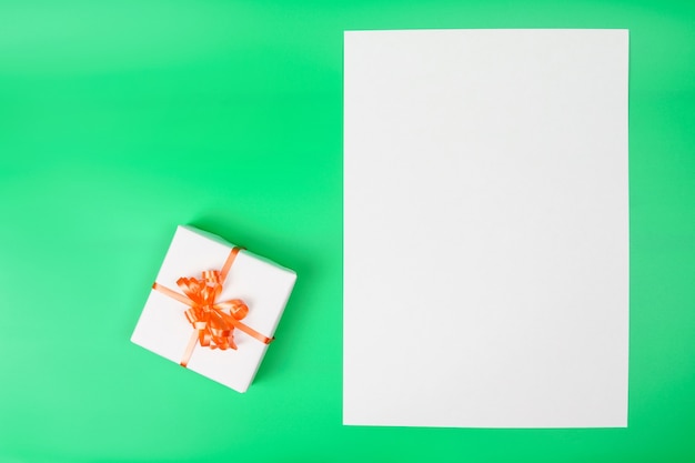 Caja de regalo blanca sobre superficie verde y tarjeta en blanco