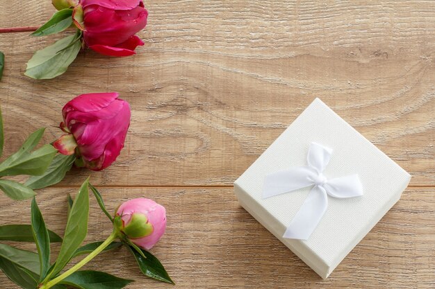 Caja de regalo blanca sobre tablas de madera decoradas con flores de peonía.