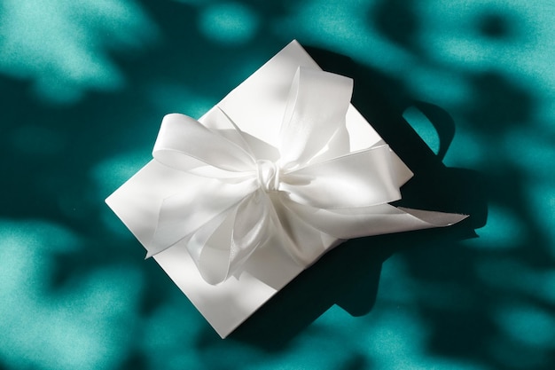 Caja de regalo blanca de vacaciones de lujo con cinta de seda y lazo sobre fondo verde esmeralda boda de lujo o regalo de cumpleaños
