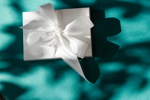 Caja de regalo blanca de vacaciones de lujo con cinta de seda y lazo sobre fondo verde esmeralda boda de lujo o regalo de cumpleaños