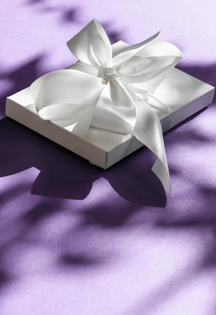 Caja de regalo blanca de vacaciones de lujo con cinta de seda y lazo sobre fondo violeta boda de lujo o regalo de cumpleaños