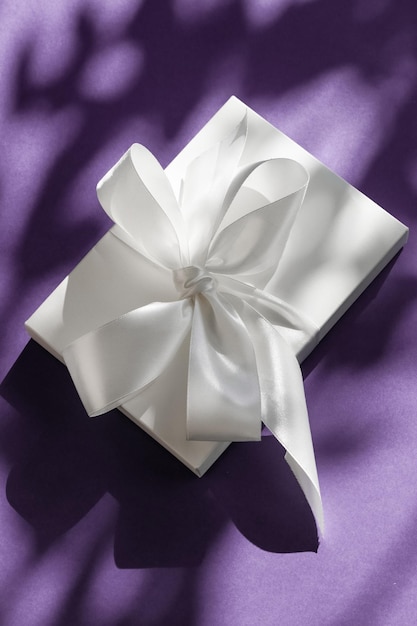 Caja de regalo blanca de vacaciones de lujo con cinta de seda y lazo sobre fondo violeta boda de lujo o regalo de cumpleaños