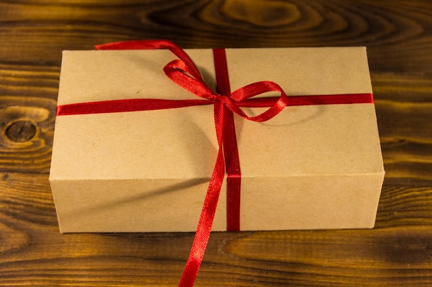 Caja de regalo de cartón con cinta roja sobre mesa de madera