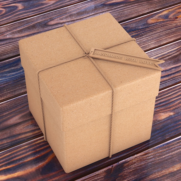 Caja de regalo de cartón con cuerda y etiqueta artesanal de madera con letrero hecho a mano con amor en una mesa de madera. Representación 3D