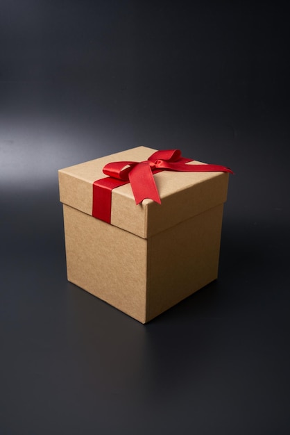 Caja de regalo de cartón marrón con una cinta roja sobre un fondo negro